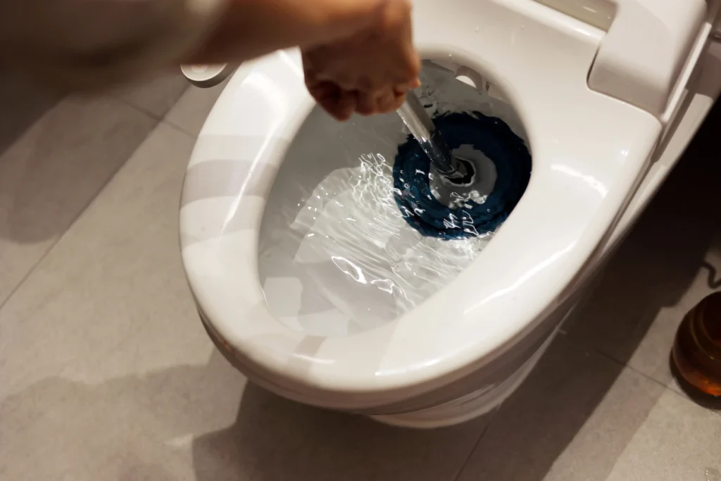 A person using a plunger to unclog a toilet